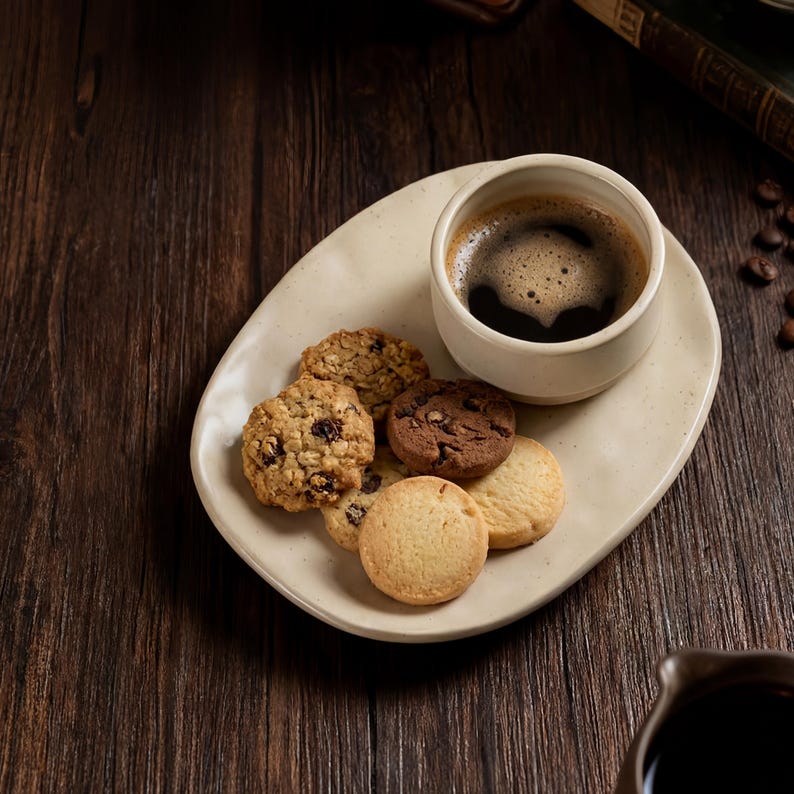 Top view of ceramic coffee cup and assorted cookies on a handmade oval stoneware plate