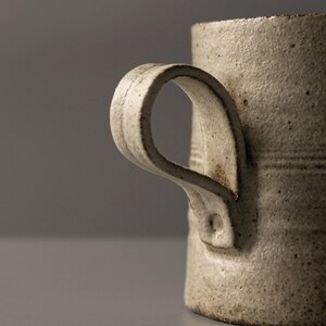 Close-up detail of the hand-shaped ceramic mug handle with natural curves and raw clay texture