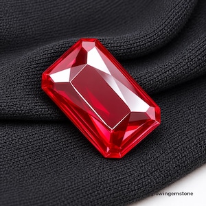 May include: A rectangular faceted red gemstone with a brilliant cut, displaying sharp edges and reflective surfaces. The stone is positioned against a dark black textured fabric background. The text glowingemstone is visible in the bottom corner.