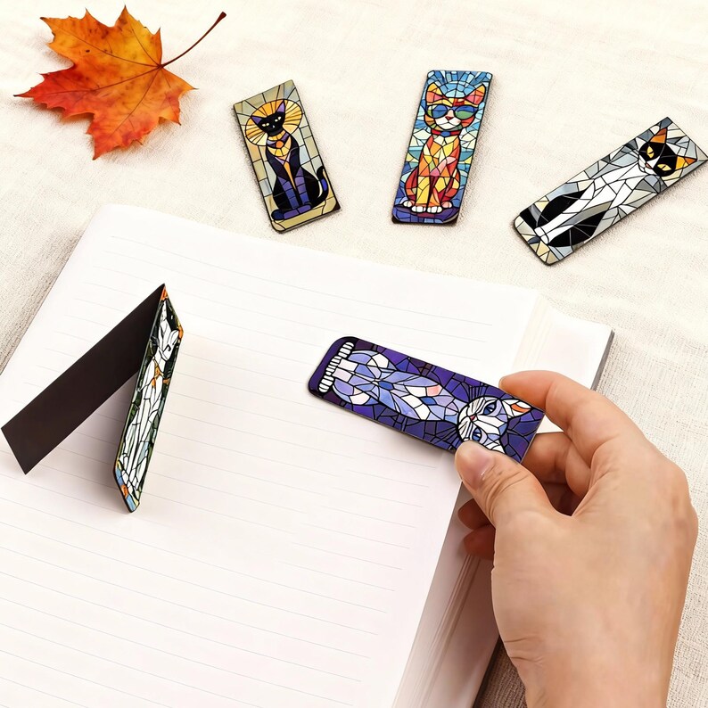 May include: A collection of cat-themed bookmarks with a stained-glass design. Each bookmark features a different cat pose and color scheme, including black, orange, and white cats. The bookmarks are rectangular and magnetic, designed to clip onto pages.