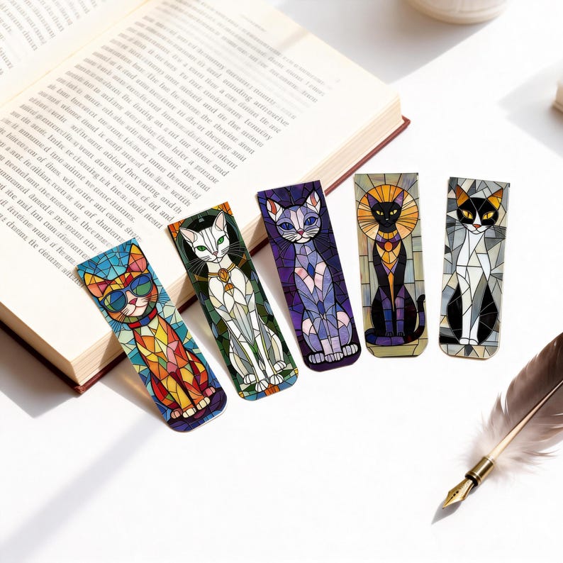 May include: Five colorful cat-themed bookmarks with stained glass designs are displayed next to an open book. The bookmarks feature various cat poses and colors, including orange, white, purple, black, and gray. A feather quill rests nearby.