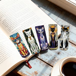 May include: A collection of five colorful cat-themed bookmarks with stained glass designs. Each bookmark features a different cat illustration with unique color palettes and patterns. The bookmarks are displayed on an open book.
