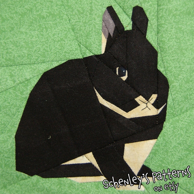 A photo of a quilt block made from this pattern.  A black Netherland Dwarf rabbit sits looking at the viewer.