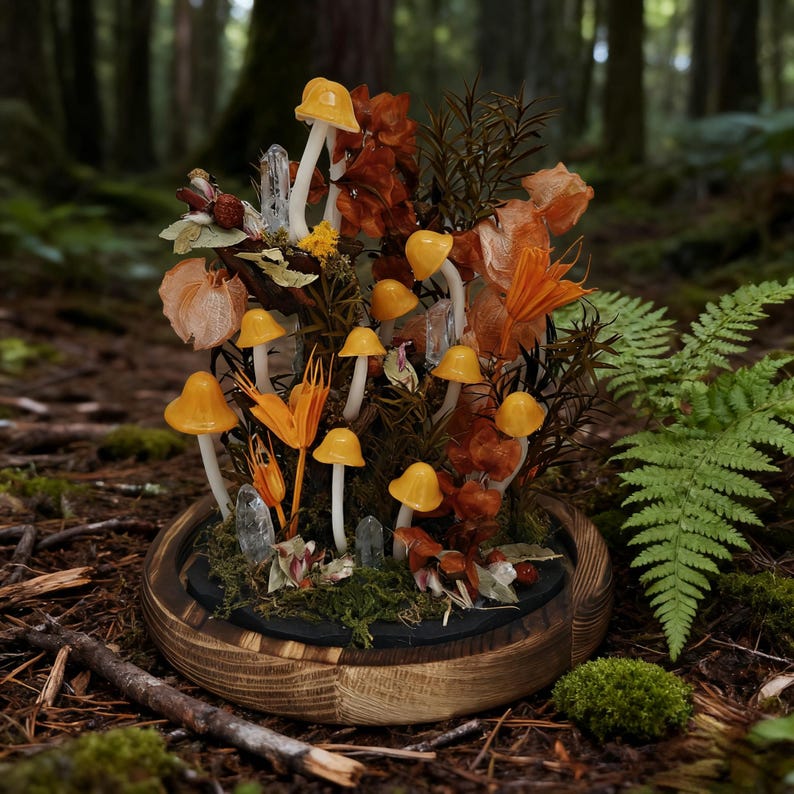 May include: A decorative terrarium featuring miniature yellow mushrooms with white stems, clear crystals, and dried orange foliage. The arrangement is set in a wooden base with a dark interior, creating a whimsical forest scene.