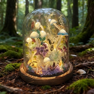 Puede incluir: Una campana de cristal sobre una base de madera alberga una escena de bosque en miniatura. Setas iluminadas con sombreros blancos y azules están rodeadas de flores secas y musgo. El fondo es un bosque borroso.