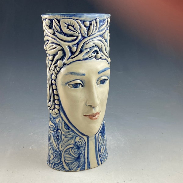 Blue and white one of a kind ceramic sculpted face vase in blue and white. 9 inches tall with hand sculpted face and elaborate hand carving