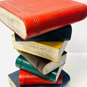 May include: A stack of colorful, decorative wooden books. The books are painted in various colors, including red, blue, green, and yellow. The edges of the pages are painted to look aged. The books are stacked on top of each other.