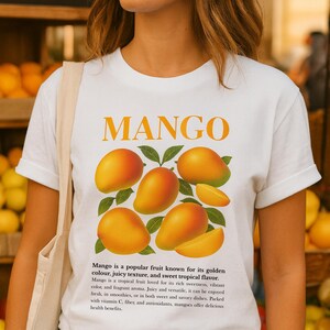 以下が含まれることがあります： マンゴーのグラフィックが特徴の白いTシャツ。デザインには、オレンジ色の「MANGO」の文字と、熟したマンゴーと緑の葉のイラストが含まれています。シャツには、果物の特性を説明するテキストも含まれています。