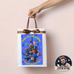 以下が含まれることがあります： 茶色のリボンとハンドルが付いた白いギフトバッグ。バッグには、漫画のキャラクターのカラフルなイラストと、青い背景に「THANK YOU FOR COMING AND MAKING MY BIRTHAY EXTRA SPECIAL」というテキストが表示されています。