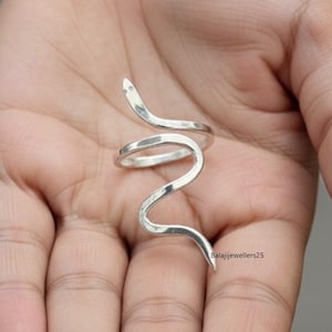 May include: A silver snake ring with a coiled body and raised head. The ring is worn on a finger and has a polished finish. The design is minimalist and elegant. The ring is suitable for everyday wear and is a stylish accessory.
