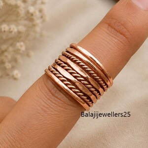May include: A stack of five copper-colored rings worn on a finger. The set includes two smooth bands, two twisted rope-textured bands, and one hammered band. The text Balajijewellers25 is visible on the lower portion of the ring stack.