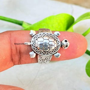 Op de afbeelding: Een zilveren schildpadring. De ring heeft een gedetailleerd schildpadontwerp met een getextureerd schild, een kleine kop en vinachtige voeten. De ring wordt op een vinger gedragen. De tekst "Balajijewellers25" is zichtbaar.