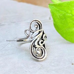 Könnte beinhalten: Ein silberner Ring mit einem verzierten, wirbelnden Design. Der Ring weist eine Reihe von miteinander verbundenen Kurven und Schlaufen auf, die ein elegantes und künstlerisches Aussehen erzeugen. Der Ring ist vor einem neutralen Hintergrund platziert, der seine komplizierten Details hervorhebt.