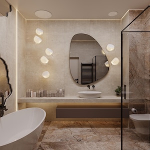 May include: A modern bathroom with a large oval mirror, a white oval sink, and a white bathtub. The walls are a light beige color, and the floor is a patterned stone. Decorative lights hang from the ceiling.