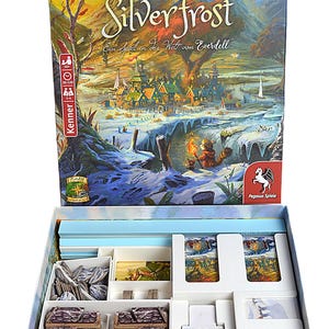 Op de afbeelding: Een bordspeldoos met de titel "Silverfrost" met een fantasielandschapsillustratie. De doos is open en onthult spelcomponenten in georganiseerde compartimenten. Het spel is voor 3-4 spelers en duurt 30-120 minuten.
