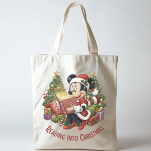 K&ouml;nnte beinhalten: Beige Tragetasche mit einer weihnachtlichen Illustration von Minnie Mouse, die ein Buch liest. Sie tr&auml;gt einen Weihnachtsmannhut und ein rotes Outfit, umgeben von Geschenken und Weihnachtsb&auml;umen. Der Text "Reading into Christmas" ist auf der Tasche aufgedruckt.