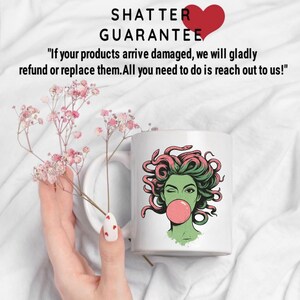May include: White ceramic mug featuring a green-skinned woman with pink hair and a bubblegum bubble. The mug has the text "SHATTER GUARANTEE" and a guarantee statement. The mug is held near pink flowers.