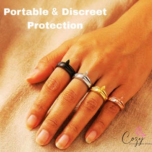 Puede incluir: Cuatro anillos en tonos negro, plata, oro y oro rosa, cada uno con un pequeño elemento en forma de punta. El texto Portable & Discreet Protection es visible en la parte superior y el texto Cozy Little Finds Store está abajo.