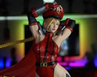 May include: A collectible figurine of a blonde character wearing a red bodysuit, a matching red cap, and a long red cape. The character has black arm guards, black thigh-high boots, and a black belt with a gold buckle. The figure is posed with arms raised.