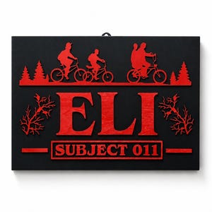 Può includere: Cartello rettangolare nero con testo e grafica rossi. Il cartello presenta il nome "ELI" e il testo "SUBJECT 011". Sono presenti anche sagome rosse di ciclisti e alberi.