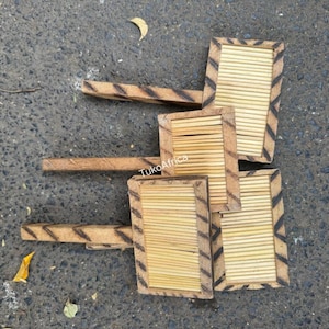 May include: A collection of handmade wooden coasters with a rectangular design. Each coaster features a light brown bamboo centre framed by a darker, patterned border. The coasters have a handle and are arranged on a textured grey surface.