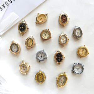 May include: A collection of small, oval and round watch faces in gold and silver tones. Each piece features a unique dial design with either Roman or Arabic numerals, metallic hands, and decorative bezels, arranged on a plain white surface.