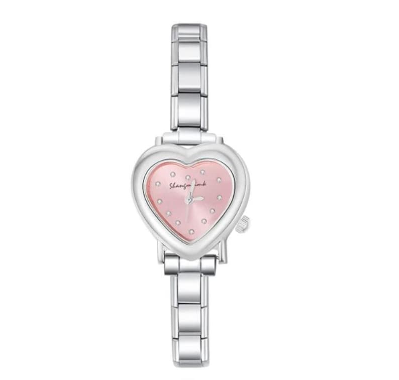 May include: A silver-toned wristwatch with a heart-shaped face and a pink dial. The watch features a linked metal band and small, decorative crystals. The watch face has the text "Shannon Lamb".