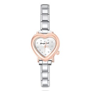 May include: A silver and rose gold wristwatch with a heart-shaped face. The watch has a silver band and a white watch face with small, round markers. The watch face has the text "Shanzin ink" in cursive.