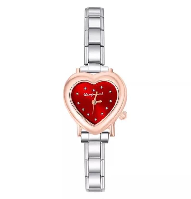 May include: A heart-shaped wristwatch with a red face and silver band. The watch face has small, sparkling accents and the text "Shining for love". The watch has a rose gold bezel and a silver link band.