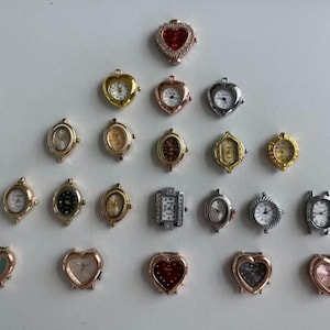 May include: A selection of small watch faces in diverse shapes, such as oval, heart, and rectangular. The watch faces have frames in gold, silver, and rose gold, with white watch faces and some with red or black detailing. Measurements are not available.