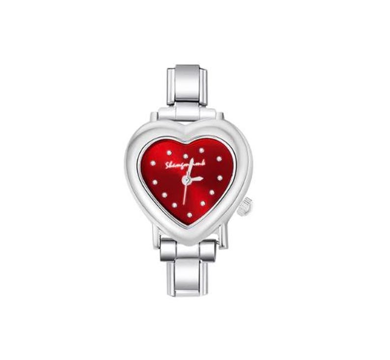 May include: A silver-toned wristwatch with a heart-shaped face. The watch face is red with white dots and the brand name. The watch has a silver band and a small crown on the side.