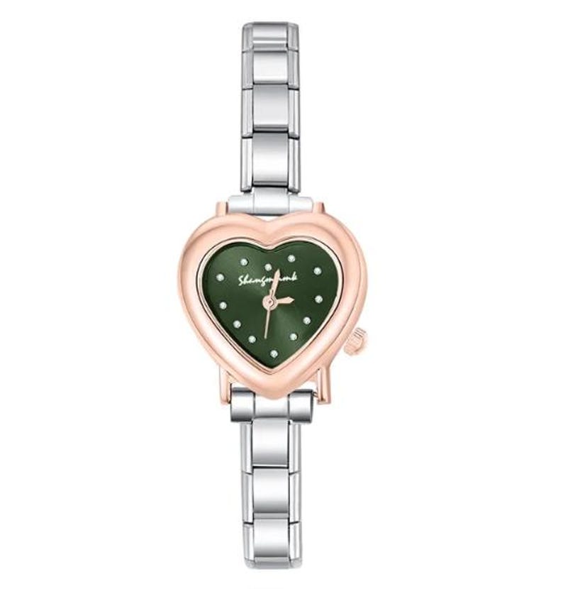 May include: A heart-shaped wristwatch with a green face and a rose gold-colored bezel. The watch has a silver-colored band and the text "Shemforbomb" is printed on the watch face. The watch hands are gold-colored.