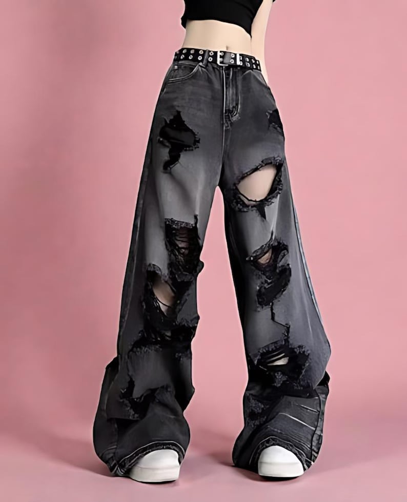 Pu&ograve; includere: Jeans neri strappati con ampi strappi e lacerazioni. I pantaloni a gamba larga presentano una cintura nera borchiata e scarpe da ginnastica bianche. I jeans hanno un aspetto sbiadito, perfetto per uno stile casual e audace.