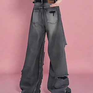 Pu&ograve; includere: Jeans neri sbiaditi a gamba larga con dettagli strappati. I jeans presentano sezioni strappate sulle gambe e tasche posteriori. I jeans hanno una vita alta e un passante per la cintura.