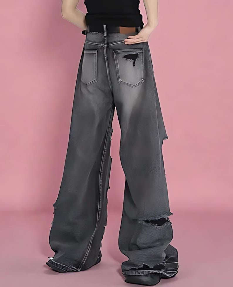 Pu&ograve; includere: Jeans neri sbiaditi a gamba larga con dettagli strappati. I jeans presentano sezioni strappate sulle gambe e tasche posteriori. I jeans hanno una vita alta e un passante per la cintura.