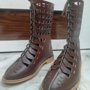 May include: A pair of brown leather boots with a unique cut-out design. The boots have a lace-up closure and a light brown sole. The open design allows for ventilation, making them suitable for warmer weather. The boots are made of leather.