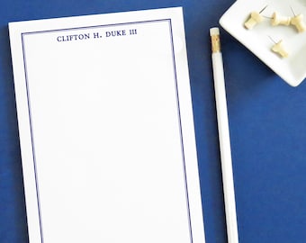 May include: A white notepad with a blue border and the text "CLIFTON H. DUKE III" at the top. A white pencil and a small white dish with four push pins are on a blue surface.