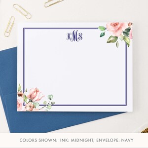 May include: A white stationery card with a navy blue border and a floral design in the corner. The card has a monogram in the center that reads "KMS". The card is shown on top of a navy blue envelope.