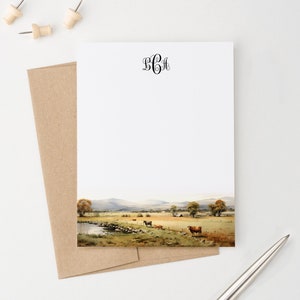 May include: A white stationery card with a black monogram "BCH" at the top. The bottom of the card features a watercolour illustration of a rural landscape with a pond, green fields, and brown cows.