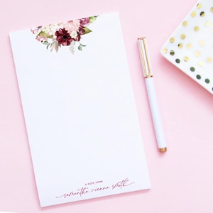 May include: A white notepad with a floral design at the top. The notepad has a burgundy floral design with pink and white flowers. The notepad has the text "A note from Samantha Vienna Smith" at the bottom.