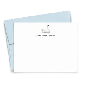 May include: A white stationery card featuring a watercolor illustration of a white swan centered above the printed name KATHERINE TAYLOR in black serif font, accompanied by a light blue envelope positioned behind the card.