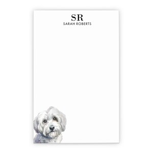 May include: A rectangular white notepad featuring the black printed initials SR above the name Sarah Roberts in a clean serif font. The bottom left corner displays a detailed watercolor illustration of a fluffy white dog with dark eyes.