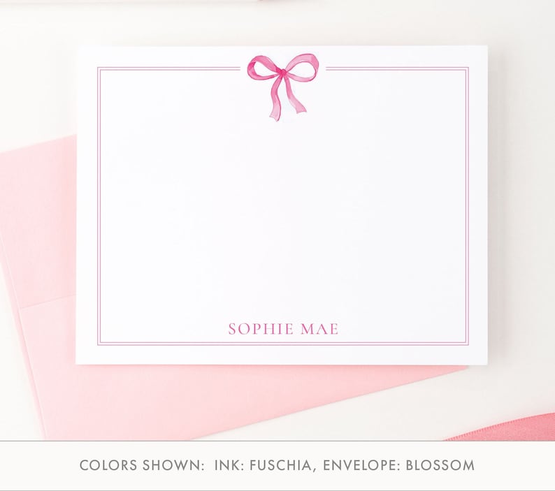 May include: A white stationery card with a pink bow and the name "SOPHIE MAE" printed in pink at the bottom. The card has a thin pink border.