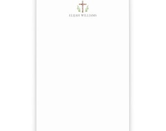 May include: White notepad with a wooden cross and green leaves design. The text "ELIJAH WILLIAMS" is printed below the design.