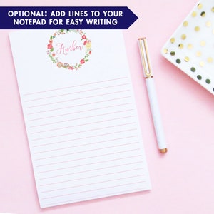 Pu&ograve; includere: Un blocco note bianco con carta rigata rosa e una ghirlanda di fiori con il nome "Amber" in lettere rosa. Il blocco note &egrave; su uno sfondo rosa con un piatto bianco con pois dorati.