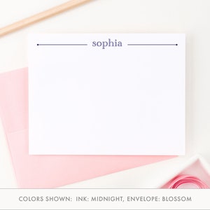 May include: A white card with a navy blue line and the name "sophia" printed on it. The card is on top of a pink envelope. The text "COLORS SHOWN: INK: MIDNIGHT, ENVELOPE: BLOSSOM" is below the card.