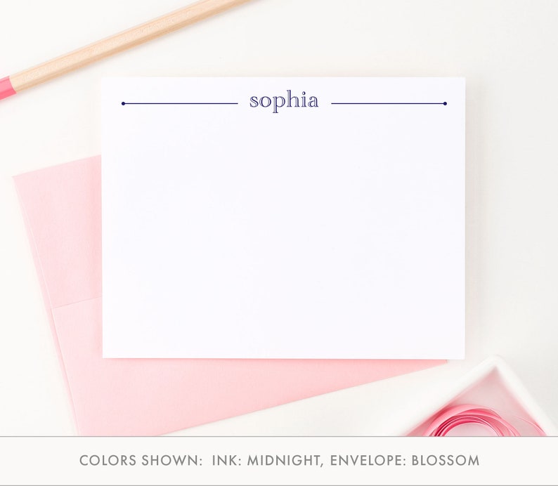 May include: A white card with a navy blue line and the name "sophia" printed on it. The card is on top of a pink envelope. The text "COLORS SHOWN: INK: MIDNIGHT, ENVELOPE: BLOSSOM" is below the card.
