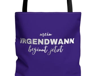 May include: A purple tote bag with black handles. The bag features the German text "mein IRGENDWANN beginnt jetzt" in white and silver lettering. The bag is made of a durable material and is suitable for carrying various items.