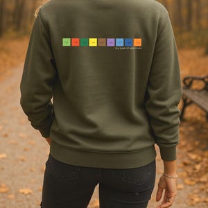 May include: An olive green sweatshirt featuring a colourful spectrum design on the back. The spectrum includes the text "U1" through "U9" in various colours, with the phrase "my type of spectrum" below.