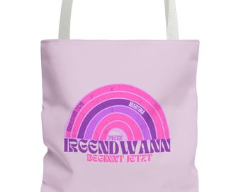 May include: A lilac tote bag with white handles. The bag displays a rainbow design in pink and purple hues, with the text "IRGENDWANN BEGINNT JETZT" and the name "Martina".